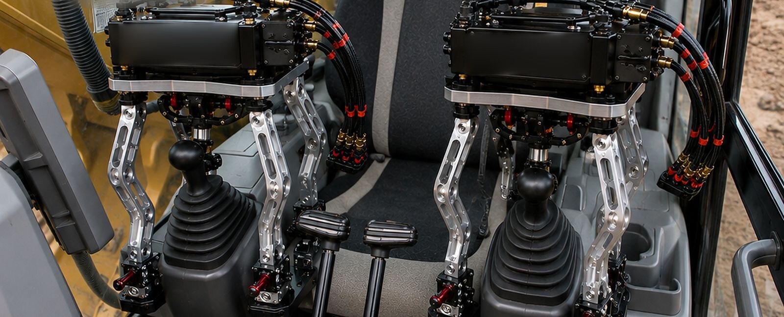 An illustration of two sealed modules on an excavator's joystick consoles, their articulated arms holding the joysticks, the seat between them.